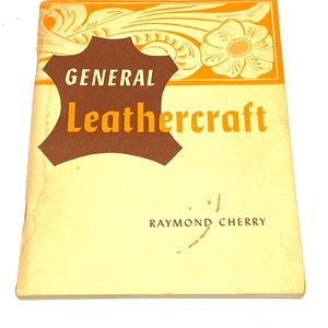 May include: A vintage book titled "General Leathercraft" by Raymond Cherry. The cover is a light yellow with orange and brown accents. The title is in bold orange letters, and the book has a decorative floral design.
