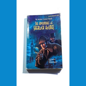 May include: A vintage paperback book cover featuring an illustration of Sherlock Holmes and Dr. Watson in a London street scene. The title of the book is "The Adventures of Sherlock Holmes" by Sir Arthur Conan Doyle. The book is complete and unabridged.