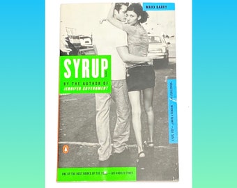 May include: A book cover with a black and white photo of a couple embracing. The book title is "Syrup" in green letters. The author is Maxx Barry. The book is described as "One of the best books of the year" by the Los Angeles Times.