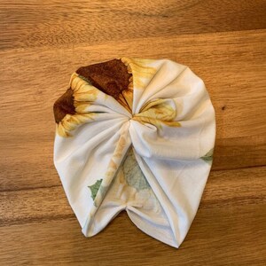 May include: White turban with a sunflower print. The turban is made of a soft, stretchy fabric and is perfect for a casual look.