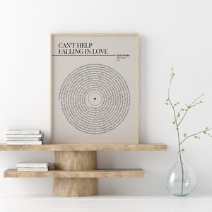 K&ouml;nnte beinhalten: Gerahmter Druck mit dem Liedtext von Elvis Presleys "Can't Help Falling in Love", kreisf&ouml;rmig angeordnet wie eine Schallplatte. Der Druck in neutralen Farben wird auf einem Holzregal pr&auml;sentiert und verleiht einen Hauch von Vintage-Charme.