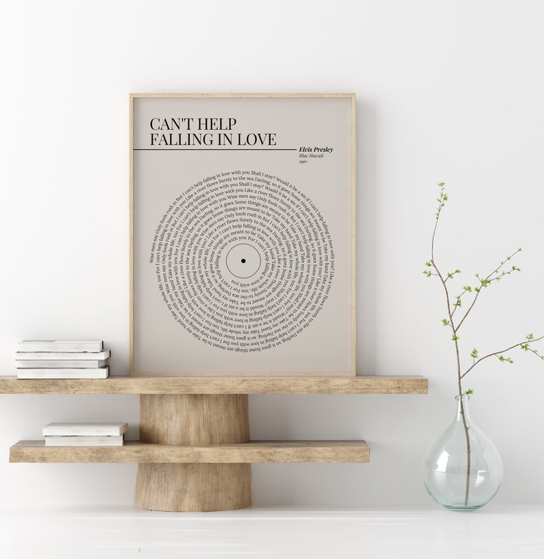 K&ouml;nnte beinhalten: Gerahmter Druck mit dem Liedtext von Elvis Presleys "Can't Help Falling in Love", kreisf&ouml;rmig angeordnet wie eine Schallplatte. Der Druck in neutralen Farben wird auf einem Holzregal pr&auml;sentiert und verleiht einen Hauch von Vintage-Charme.