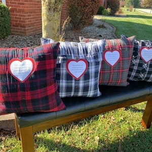 May include: Four plaid pillow covers with red and black plaid, gray and white plaid, and black and white plaid. Each pillow cover has a white heart-shaped patch with a handwritten message inside.