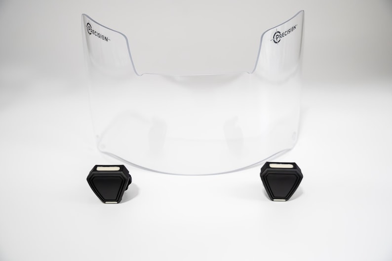 May include: A clear, curved visor with the word "PRECISION" printed on each side. Two black, geometric-shaped components are positioned below the visor. The items are set against a white background.