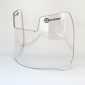 May include: A clear, curved visor with the word "PRECISION" printed in black. The visor has a rounded shape with a cut-out section and two small holes. The visor is made of transparent plastic.