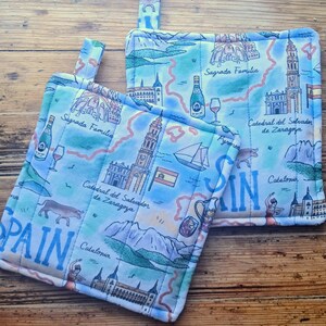 May include: Two quilted pot holders with a light blue map design featuring Spanish landmarks like Sagrada Familia and Catedral del Salvador de Zaragoza. The word "SPAIN" is prominently displayed.