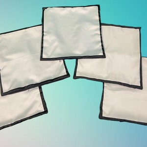Op de afbeelding: Vijf witte kussenhoezen met zwarte bies. De kussenhoezen zijn in een halve cirkel gerangschikt.