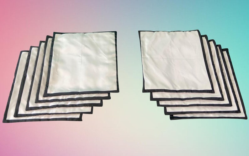 Op de afbeelding: Een set van tien witte kussenhoezen met zwarte bies. De hoezen zijn gestapeld in twee stapels van vijf.