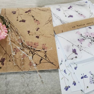 May include: A set of stationery featuring a floral design. The paper is brown with a delicate floral pattern and the envelopes are white with a light pink floral pattern. The envelopes have a brown label with the text "Letters Written Well".