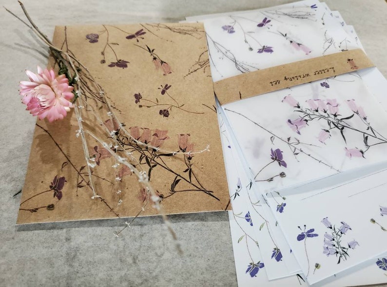 May include: A set of stationery featuring a floral design. The paper is brown with a delicate floral pattern and the envelopes are white with a light pink floral pattern. The envelopes have a brown label with the text "Letters Written Well".