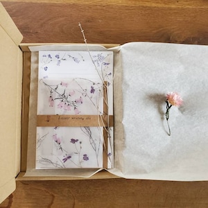 May include: A brown cardboard box with a white tissue paper lining. The box contains a letter writing set with floral patterned paper and envelopes. The set is labeled "Letter writing set".