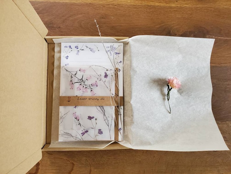 May include: A brown cardboard box with a white tissue paper lining. The box contains a letter writing set with floral patterned paper and envelopes. The set is labeled "Letter writing set".