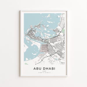 May include: A framed map print of Abu Dhabi, UAE, featuring a detailed street layout in black and white against a light blue and pink background. The city name and coordinates are printed at the bottom.
