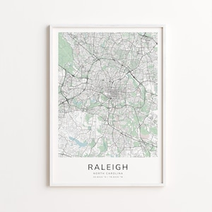 May include: A framed map print of Raleigh, North Carolina, featuring a detailed network of roads and green spaces. The city name is displayed in a clean font at the bottom, along with the coordinates 35.8324° N / 78.6429° W. The map is set against a white background.