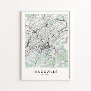 May include: A framed map print of Knoxville, Tennessee, featuring a detailed street layout in black and white. Green and light blue areas represent parks and waterways. The city name and coordinates are printed at the bottom.