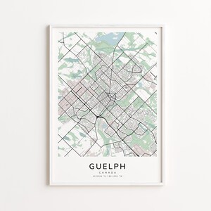 May include: A framed map print of Guelph, Canada, showing a detailed street layout in black lines against a light background with green and pink accents. The city name and coordinates are printed at the bottom.