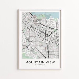 May include: A framed map print of Mountain View, California, featuring a detailed street layout in black lines against a light blue and green background. The city name and coordinates are printed at the bottom.