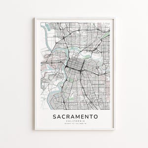 May include: A framed map print of Sacramento, California, featuring a detailed street grid and the Sacramento River. The map is in black and white with light blue water features. The city name and coordinates are printed at the bottom.