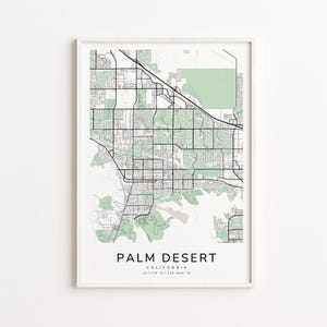 May include: A framed map print of Palm Desert, California, featuring a detailed street grid and green shaded areas. The text "PALM DESERT" is centered at the bottom, with the state and coordinates below. The print is in a white frame.