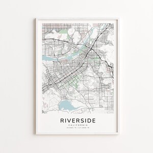 May include: A framed map print of Riverside, California, featuring a detailed street layout in black and gray. The map includes the city's roads, parks, and waterways, with the city name and coordinates displayed at the bottom.