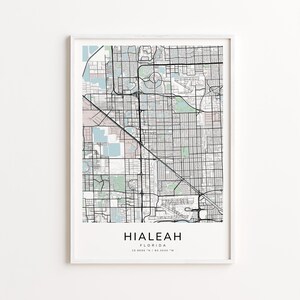 May include: A framed map print of Hialeah, Florida, featuring a detailed street grid in black lines against a light background with pastel green and pink accents. The city name is printed in a bold, sans-serif font at the bottom.