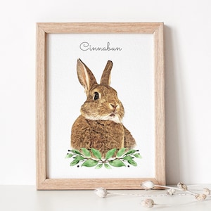 Watercolor bunny portrait displayed in a wooden frame. The bunny has a brown coat. Below the bunny portrait flowers are displayed.