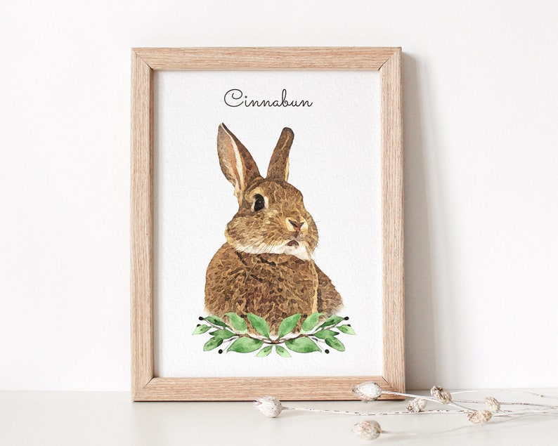 Watercolor bunny portrait displayed in a wooden frame. The bunny has a brown coat. Below the bunny portrait flowers are displayed.