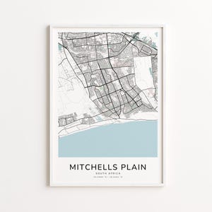 May include: A framed map print of Mitchells Plain, South Africa. The map features a detailed black and white depiction of the city's layout, with a light blue section representing the coastline. The text "MITCHELLS PLAIN" is centered at the bottom.