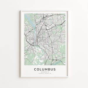 May include: A framed map print of Columbus, Georgia, featuring a detailed black and white street layout over a light green and white background. The city name and coordinates are printed at the bottom.