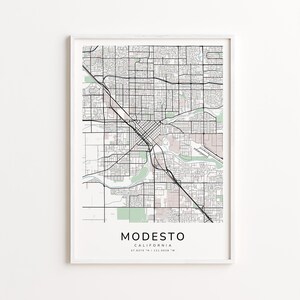 May include: A framed map print of Modesto, California, featuring a detailed street grid and surrounding areas. The map is in black and white with light pink accents for parks and waterways. The city name and coordinates are printed at the bottom.