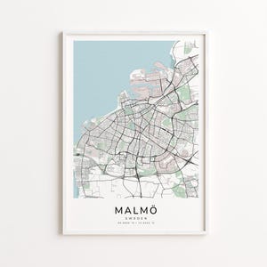 May include: A framed map print of Malmö, Sweden, in a minimalist style. The map features a detailed street layout in black and white, with a light blue sea and pale pink land areas. The city name and coordinates are printed at the bottom.