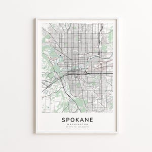 May include: A framed map print of Spokane, Washington, featuring a detailed black and white grid of streets and roads. Green areas represent parks and natural spaces. The city name is printed in a bold font at the bottom, with the state and coordinates below.