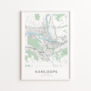 May include: A framed map print of Kamloops, Canada, in a minimalist style. The map features black lines representing roads and streets, with light green areas for parks and forests. The city name and coordinates are printed in black at the bottom.