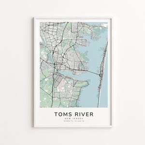 May include: A framed map print of Toms River, New Jersey, showing a detailed street layout in black and white. The map includes the town's waterways in a light blue colour, with the text "TOMS RIVER" at the bottom.