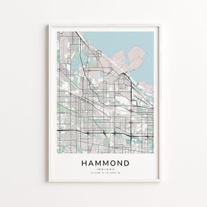 May include: A framed map print of Hammond, Indiana, featuring a detailed street layout in black lines against a light background. The map includes the city's name and coordinates at the bottom. The top portion shows a light blue area representing Lake Michigan.