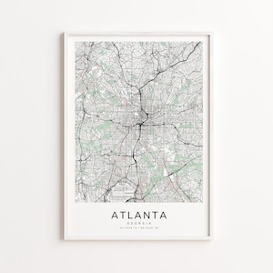 May include: A framed map print of Atlanta, Georgia, featuring a detailed street and road network in black and white. The city's name is printed in a clean font at the bottom, with the coordinates 33.7628° N / 84.4226° W.