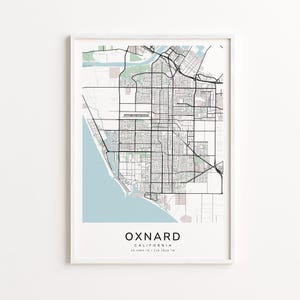 May include: A framed map print of Oxnard, California, in a minimalist style. The map features a detailed street grid, with a light blue coastal area and green accents. The city name and coordinates are printed at the bottom.