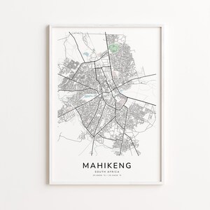 May include: A framed map print of Mahikeng, South Africa, in monochrome. The map shows the city's roads and buildings. The city name and coordinates are printed at the bottom. The frame is white.