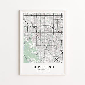 May include: A framed map print of Cupertino, California, featuring a detailed street grid in black lines against a light background. The print includes the city's name and coordinates, with green areas representing parks or natural features.