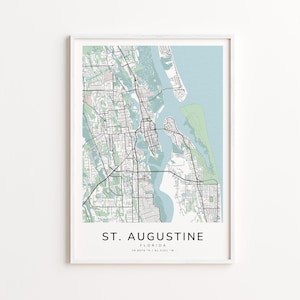 May include: A framed map print of St. Augustine, Florida, featuring a detailed street layout in black lines against a light green and blue background. The city name and coordinates are printed in a clean, modern font.