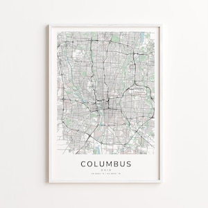 May include: A framed map print of Columbus, Ohio, featuring a detailed black and white street grid. The city name is centered at the bottom, with latitude and longitude coordinates below. The map is set against a white background.