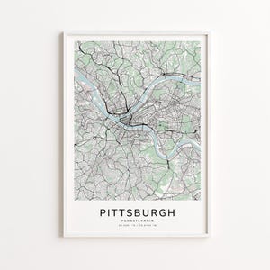 May include: A framed map print of Pittsburgh, Pennsylvania, showing a detailed street and river network in black and light blue against a pale green and white background. The city name is printed in a bold, sans-serif font at the bottom.