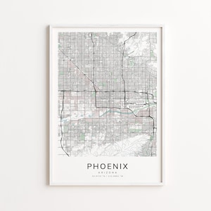 May include: A framed map print of Phoenix, Arizona, featuring a detailed street grid in black and gray. The city name is centered at the bottom in a clean, sans-serif font, with the state and coordinates below. The print is encased in a white frame.