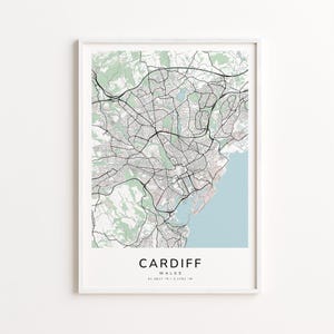 May include: A framed map print of Cardiff, Wales, featuring a detailed street layout in black lines against a light background. Green areas represent parks and natural spaces, with a light blue section indicating the coastline. The city name is printed in a bold font.