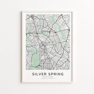 May include: A framed map print of Silver Spring, Maryland, featuring a detailed street layout in black lines against a light green and white background. The text "Silver Spring" is centered at the bottom, with coordinates below.
