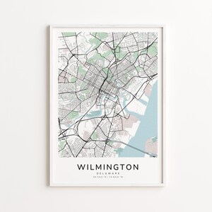 May include: A framed map print of Wilmington, Delaware, featuring a detailed street layout in black lines against a white background. Green and blue areas represent parks and water bodies. The city name is centered at the bottom.