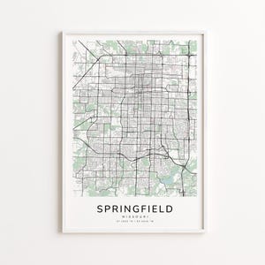 May include: A framed map print of Springfield, Missouri, featuring a detailed black and white street grid with green shaded areas representing parks and green spaces. The city name is centered at the bottom in a clean, modern font.