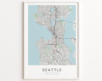 May include: Framed print of a map of Seattle, Washington, with a light blue background. The map features black lines representing streets and roads, with green areas for parks and water. The city name and coordinates are printed in black at the bottom.