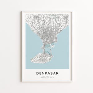 May include: A framed map print of Denpasar, Indonesia. The map shows a detailed grayscale depiction of the city's layout against a light blue background. The city name and coordinates are printed at the bottom, in a minimalist style.