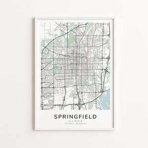 May include: A framed map print of Springfield, Illinois, featuring a detailed black and white street grid with green and blue accents. The city name and state are printed in a clean, modern font at the bottom. Coordinates are also included.
